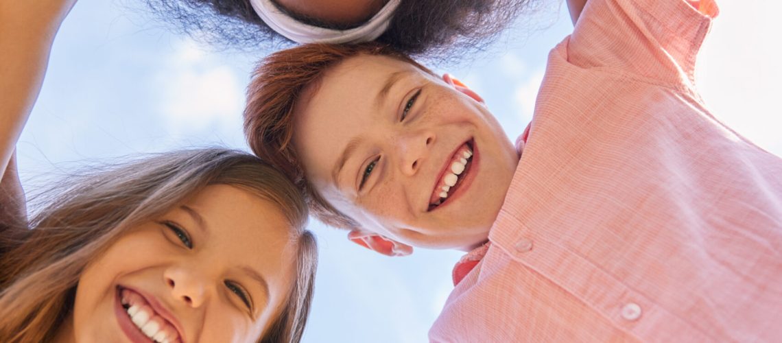 From below of group of multiethnic teen friends hugging and looking at camera on background of sky